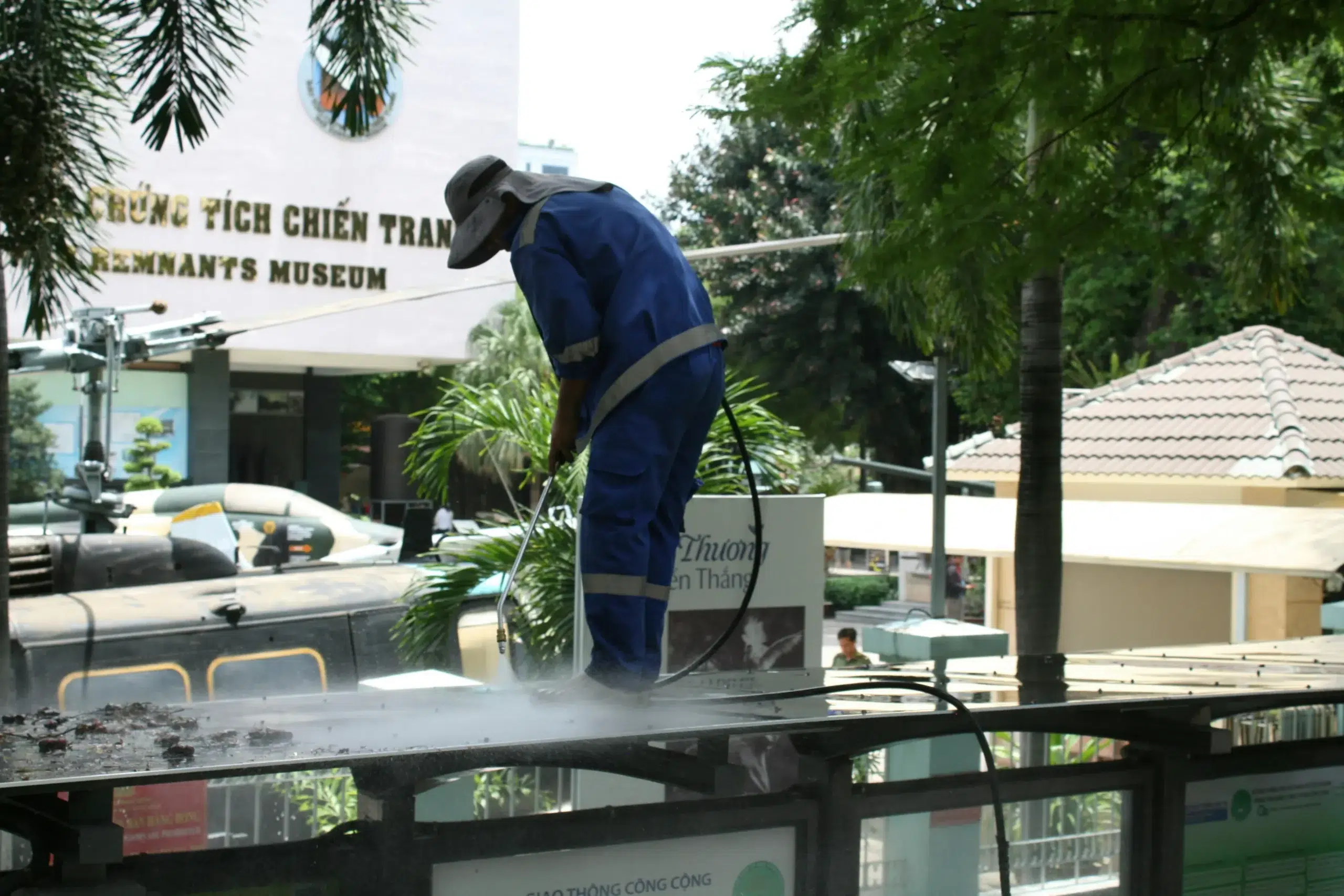 Worker pressure-washing a bus shelter roof near the War Remnants Museum