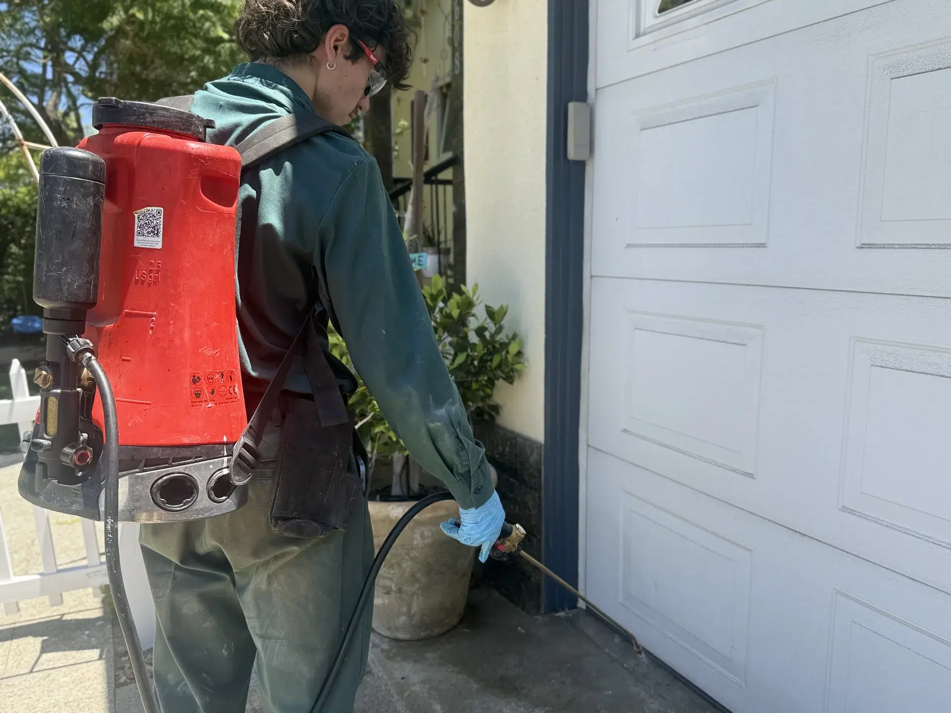 Anaheim pest control technician carrying a backpack sprayer by a garage